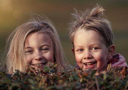Zwei Kinder lächeln glücklich in die Kamera. Burnout und Stress Coaching.