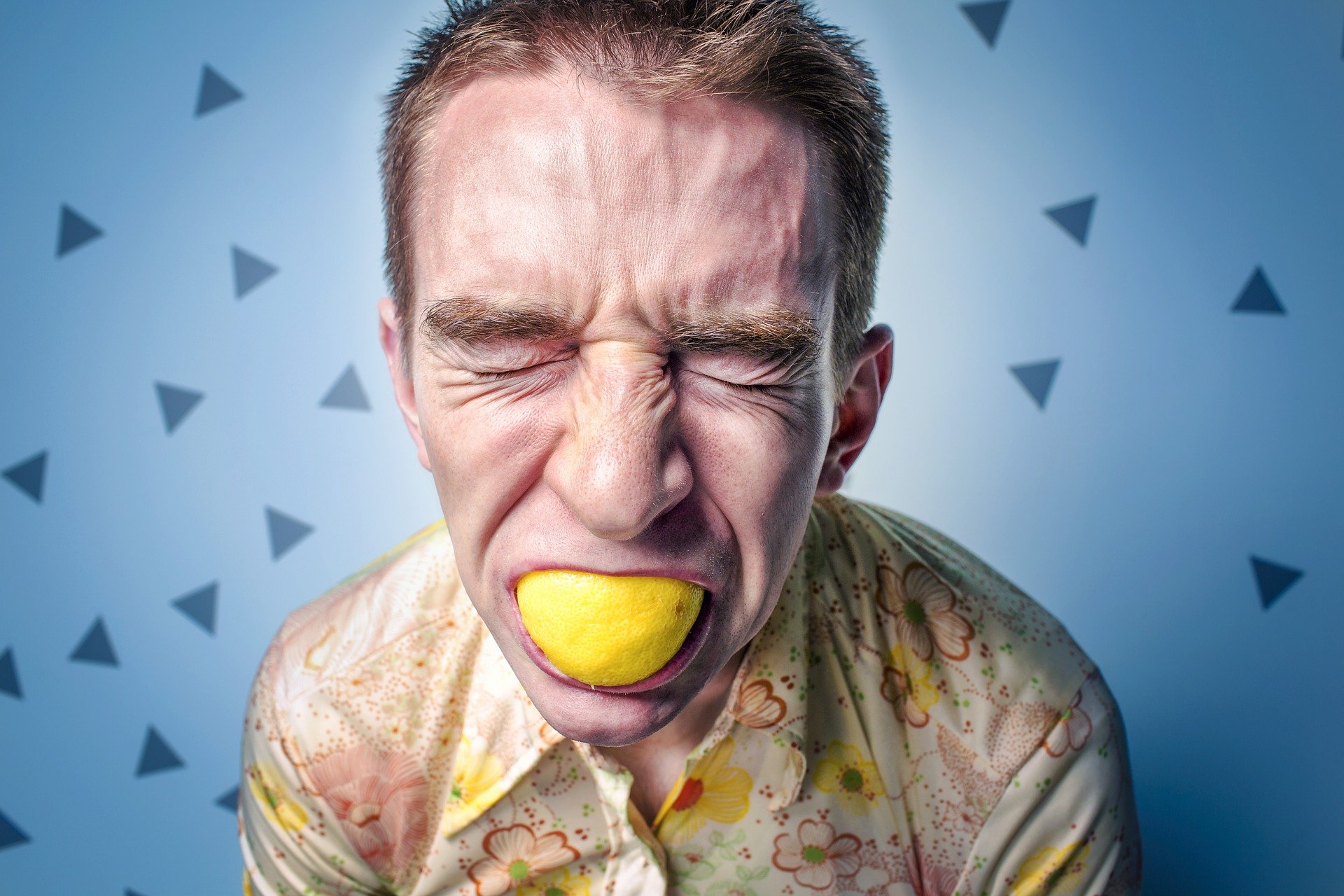 A man makes a face. He's just biting into a lemon.
