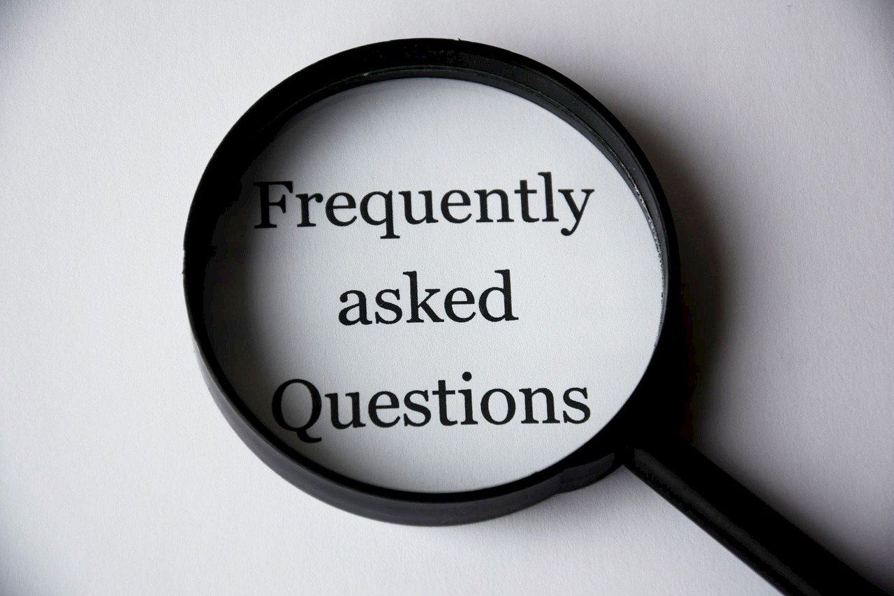Eine Lupe, die einen Text vergrößert. Darin steht Frequently asked questions. Die meistgestellten Fragen Coaching. FAQ Coaching.