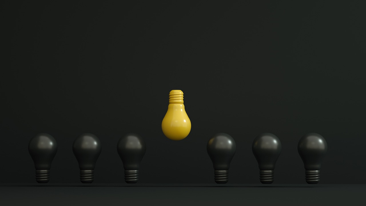 Eine gelbe Glühbirne, die sich von schwarzen Glühbirnen abhebt. Führungskompetenzentwicklung durch Coaching.